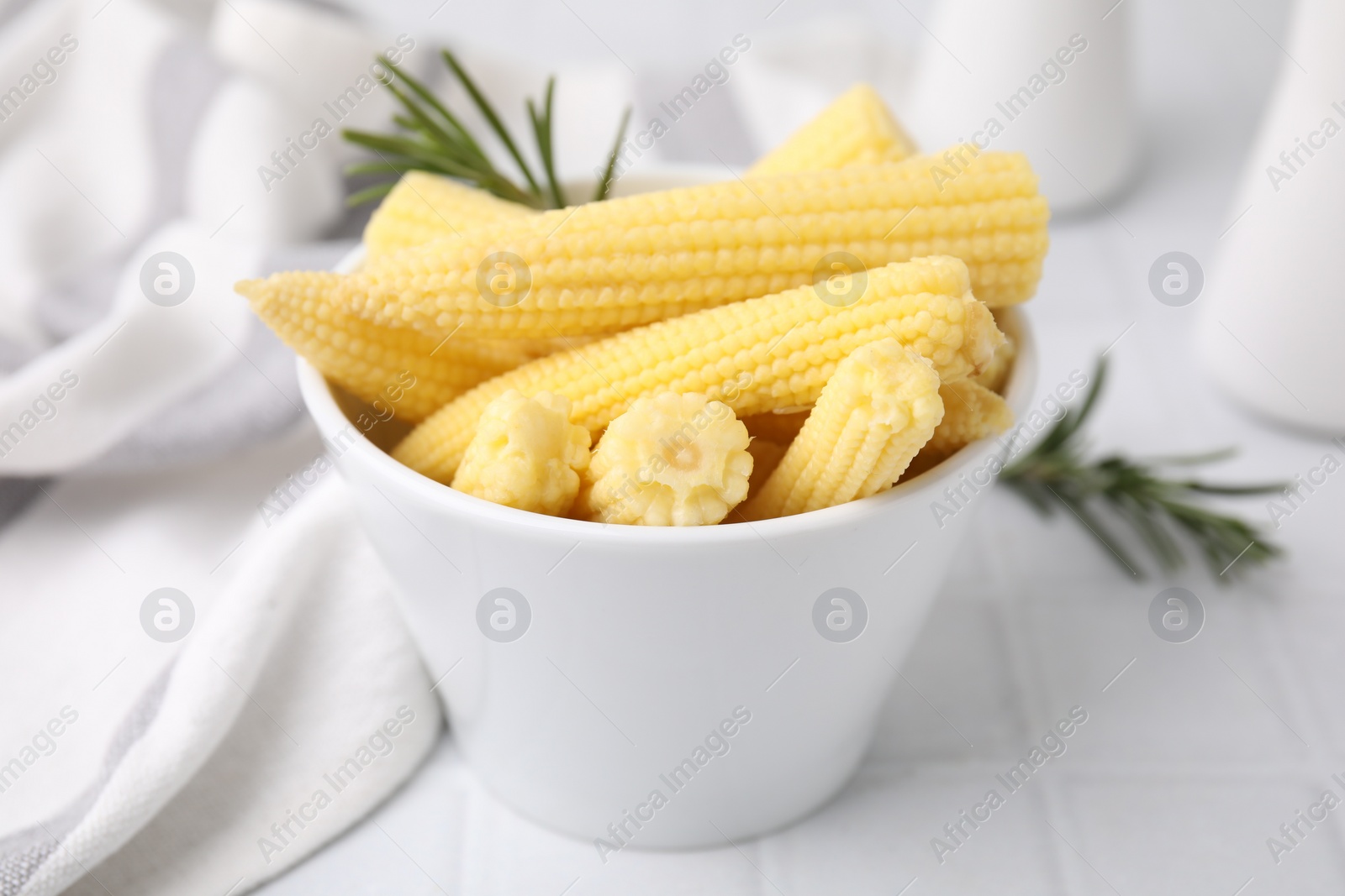 Photo of Tasty fresh yellow baby corns in bowl on white tiled table