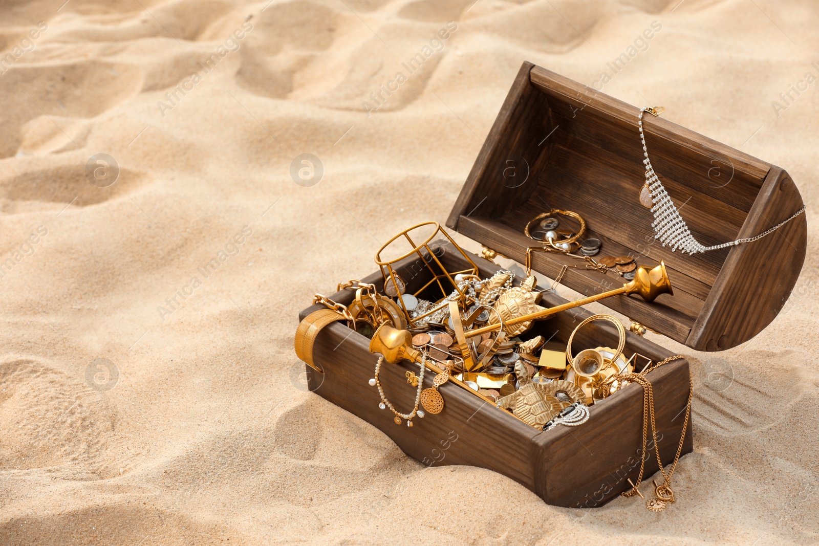 Photo of Open wooden treasure chest on sand, space for text