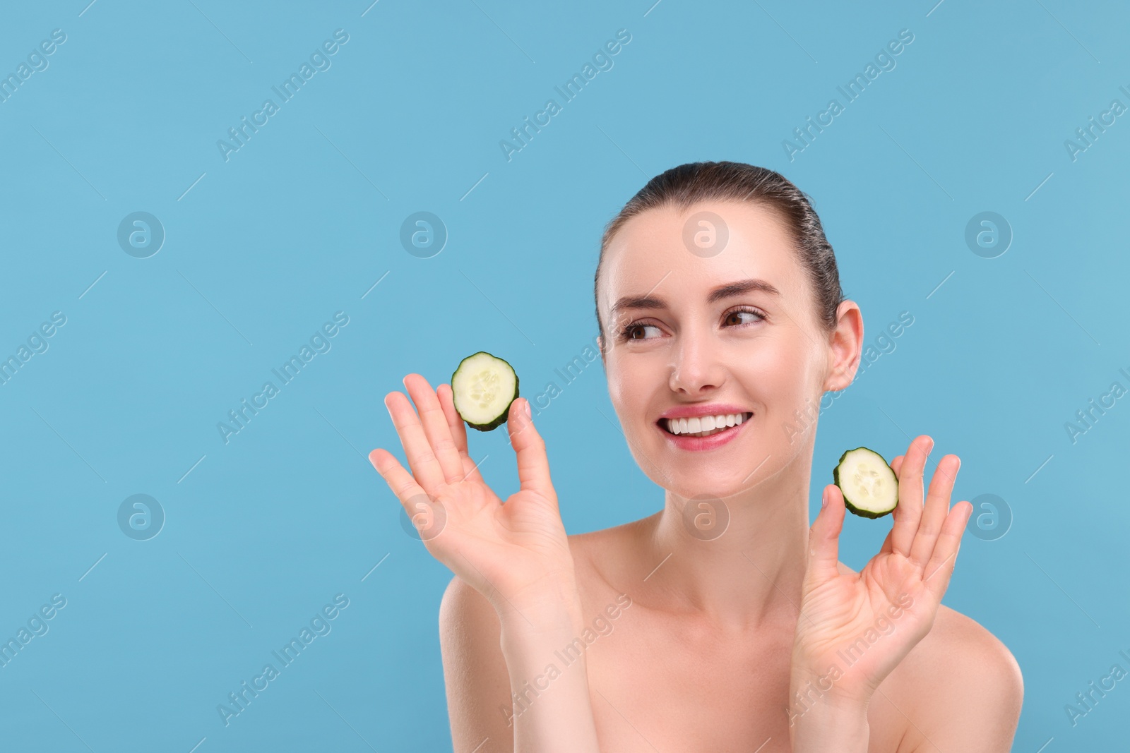 Photo of Beautiful woman with pieces of cucumber on light blue background, space for text