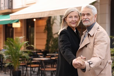 Photo of Affectionate senior couple dancing together on city street, space for text