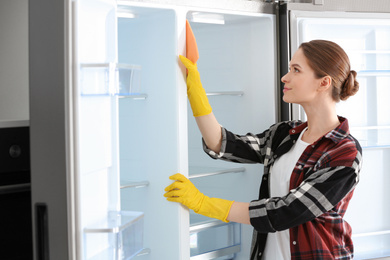 Woman in rubber gloves cleaning refrigerator at home