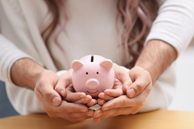 Photo of Couple holding piggy bank at table, closeup