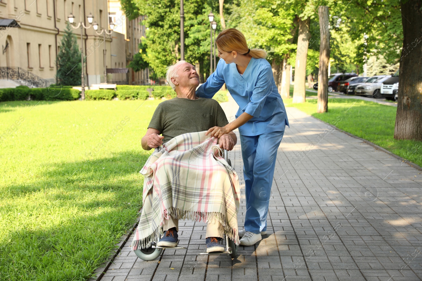 Photo of Happy nurse assisting elderly man in wheelchair at park