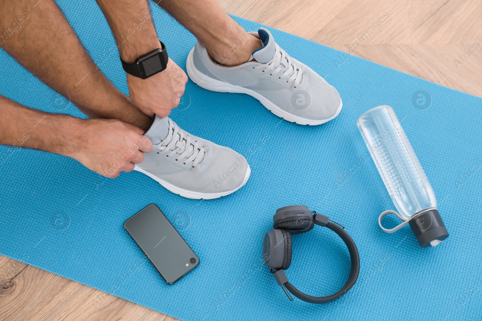 Photo of Above view of man putting on sneakers, yoga mat, bottle, smartphone and headphones