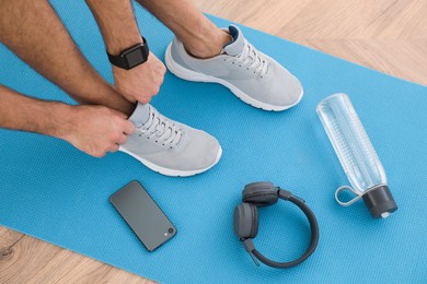 Above view of man putting on sneakers, yoga mat, bottle, smartphone and headphones