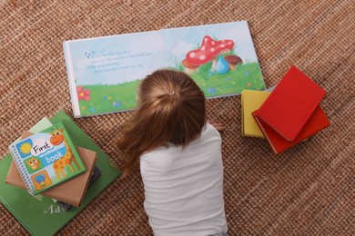 Photo of Cute little girl reading book on floor, top view
