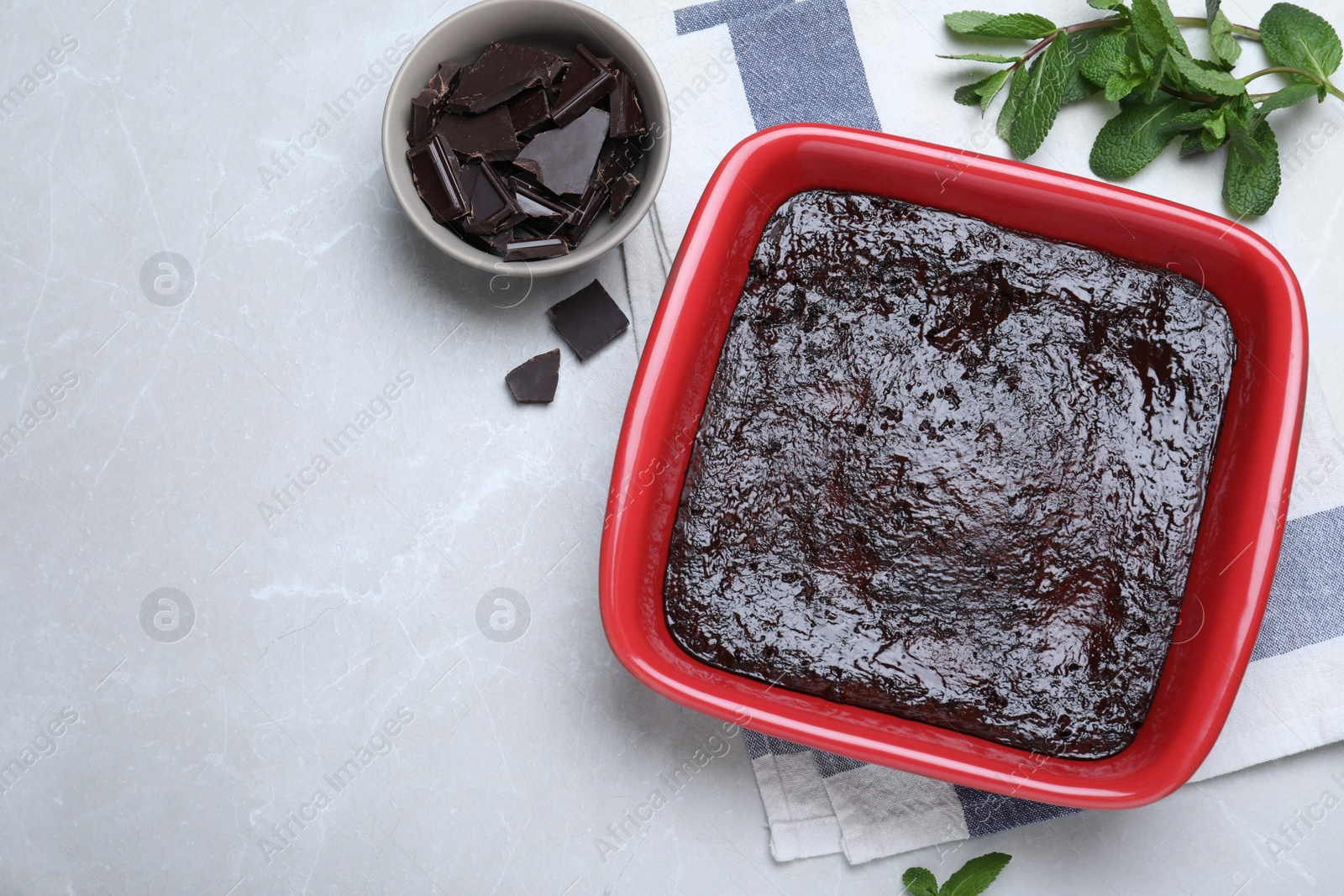 Photo of Delicious brownie in baking dish, pieces of chocolate and fresh mint on light table, flat lay. Space for text