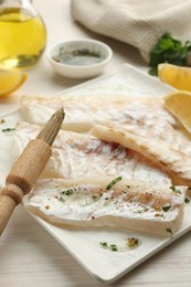 Photo of Fresh raw cod fillets with spices and brush on white wooden table, closeup