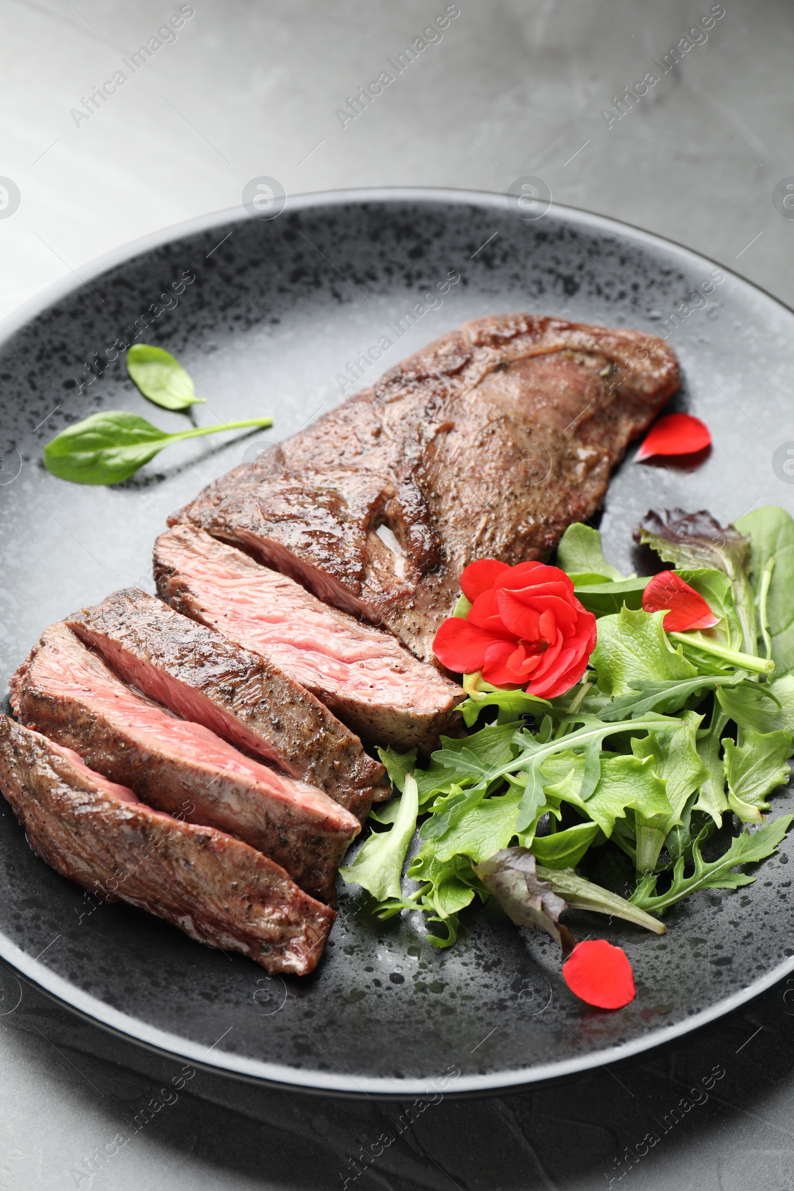 Photo of Pieces of delicious grilled beef meat and greens on table, closeup