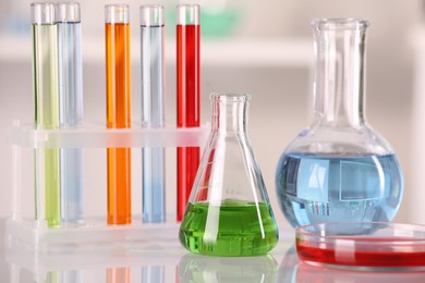 Laboratory analysis. Glass flasks, Petri dish and test tubes with liquids on white table against blurred background, closeup