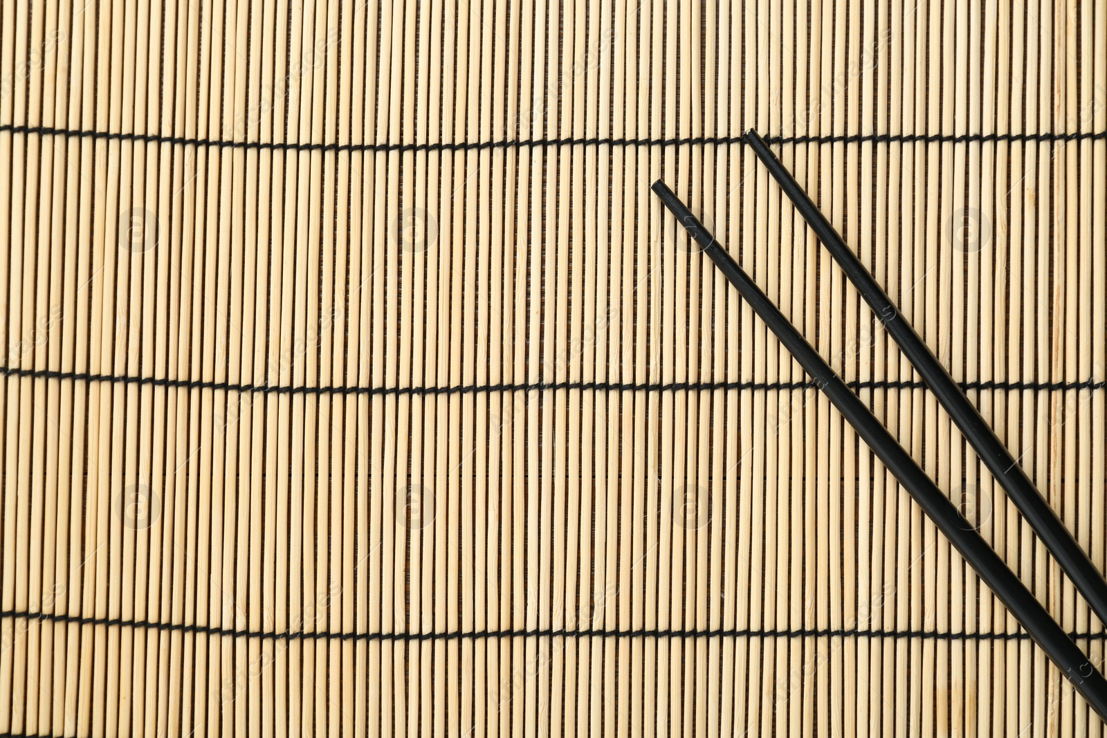 Photo of Pair of black chopsticks on bamboo mat, top view. Space for text