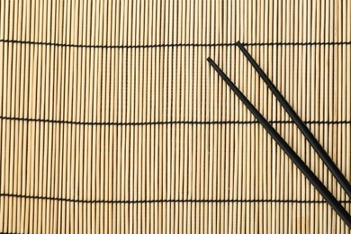 Photo of Pair of black chopsticks on bamboo mat, top view. Space for text