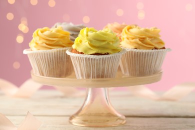 Stand with tasty cupcakes on white wooden table against blurred lights