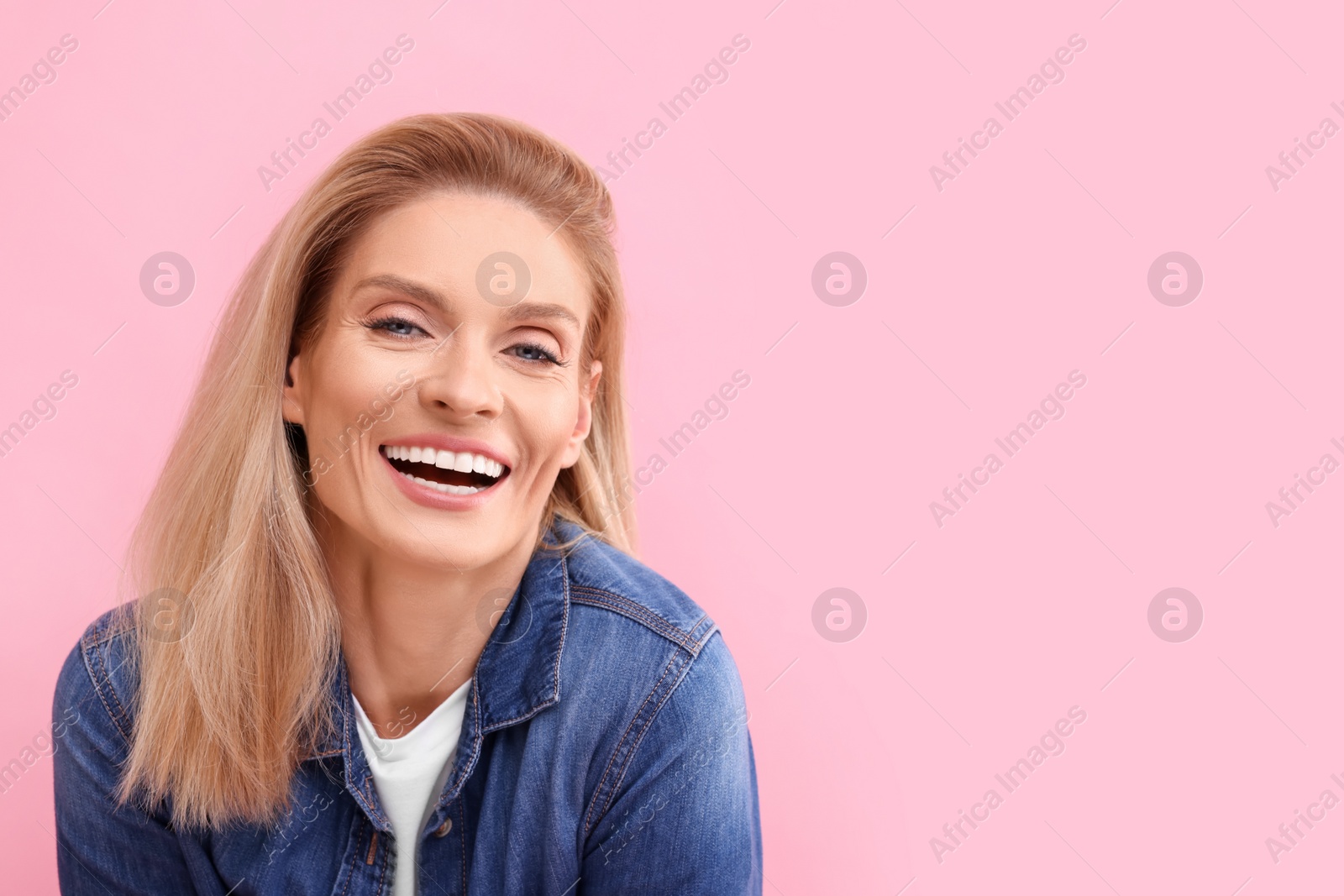 Photo of Portrait of smiling middle aged woman with blonde hair on pink background. Space for text