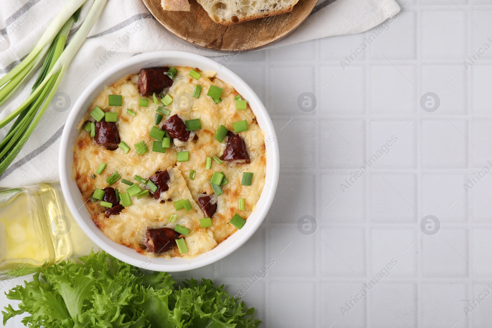 Photo of Tasty sausage casserole in baking dish served on white tiled table, flat lay. Space for text