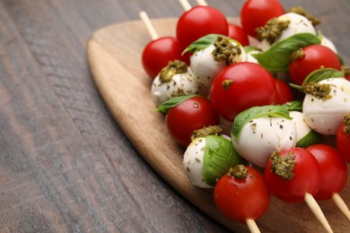 Caprese skewers with tomatoes, mozzarella balls, basil and pesto sauce on wooden table, closeup. Space for text