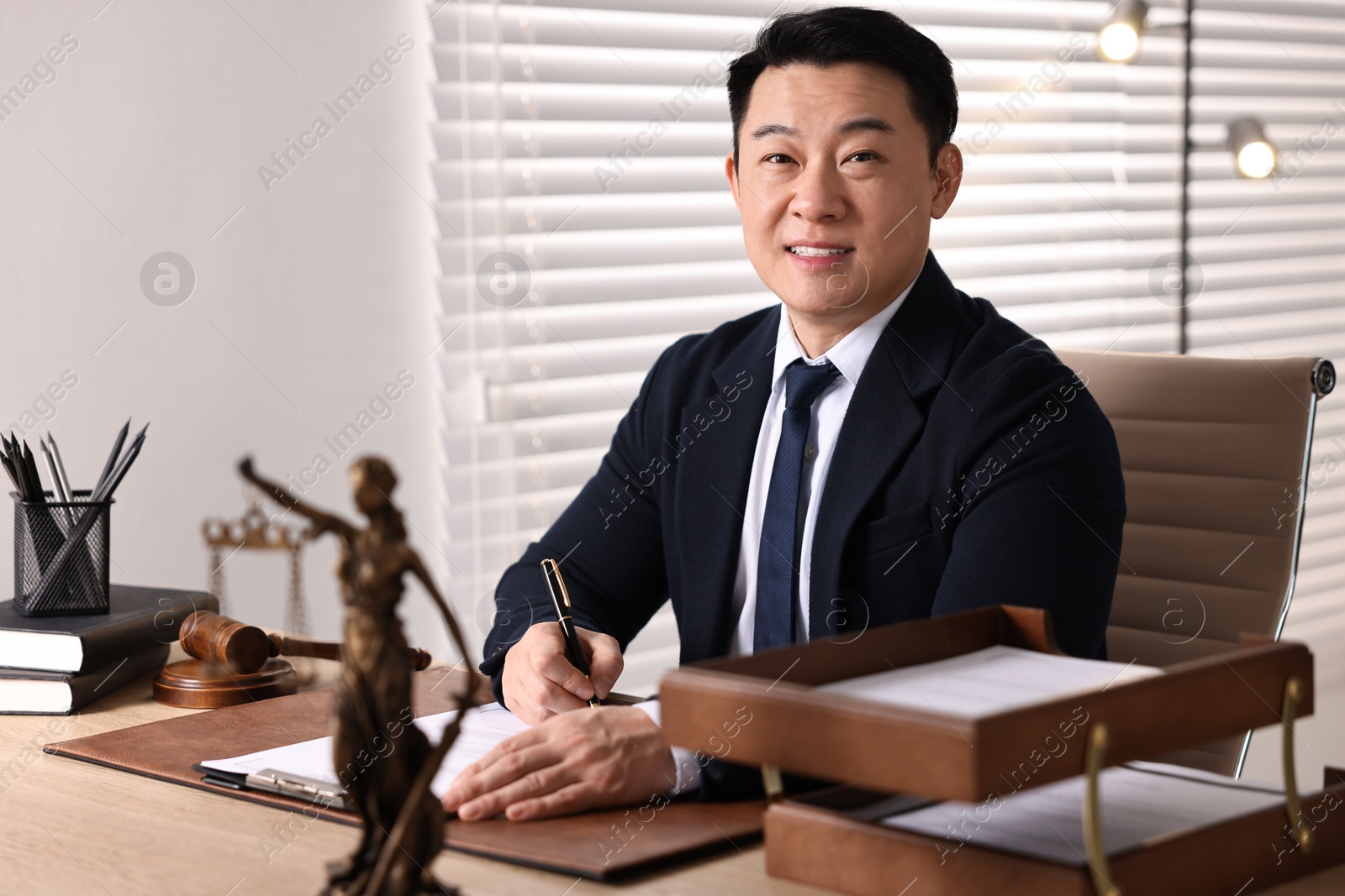 Photo of Happy notary writing notes at wooden table in office