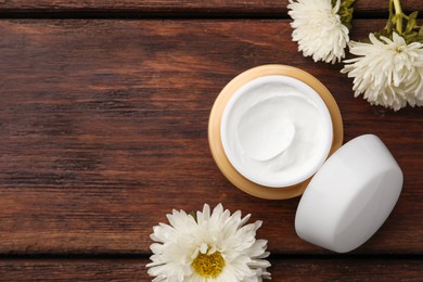 Photo of Jar of face cream and flowers on wooden table, flat lay. Space for text