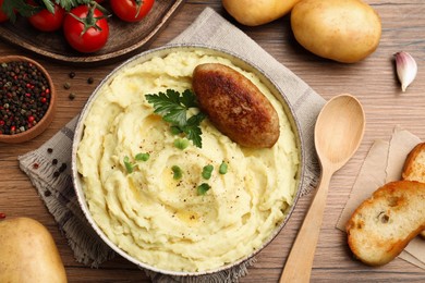 Bowl of tasty mashed potatoes with parsley, black pepper and cutlet served on wooden table, flat lay