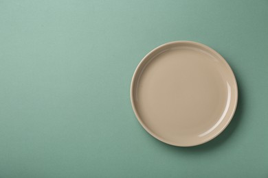 Photo of Clean beige plate on light green background, top view. Space for text