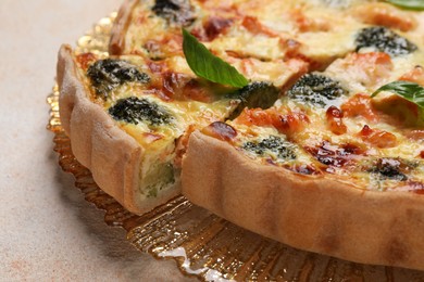 Delicious homemade quiche with salmon and broccoli on beige table, closeup