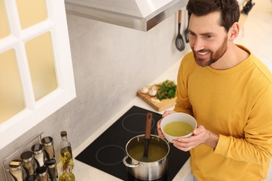 Man with bowl of delicious soup in kitchen, above view
