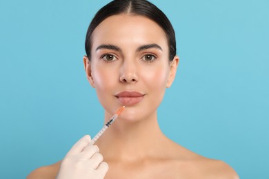 Photo of Doctor giving lips injection to young woman on light blue background. Cosmetic surgery