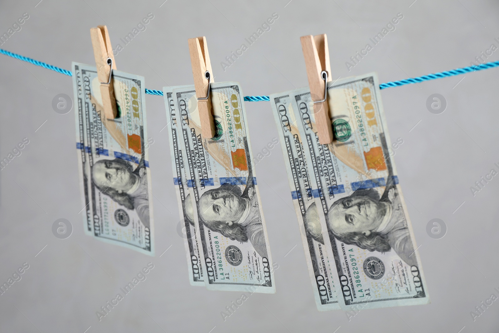 Photo of Dollar banknotes hanging on rope against light grey background