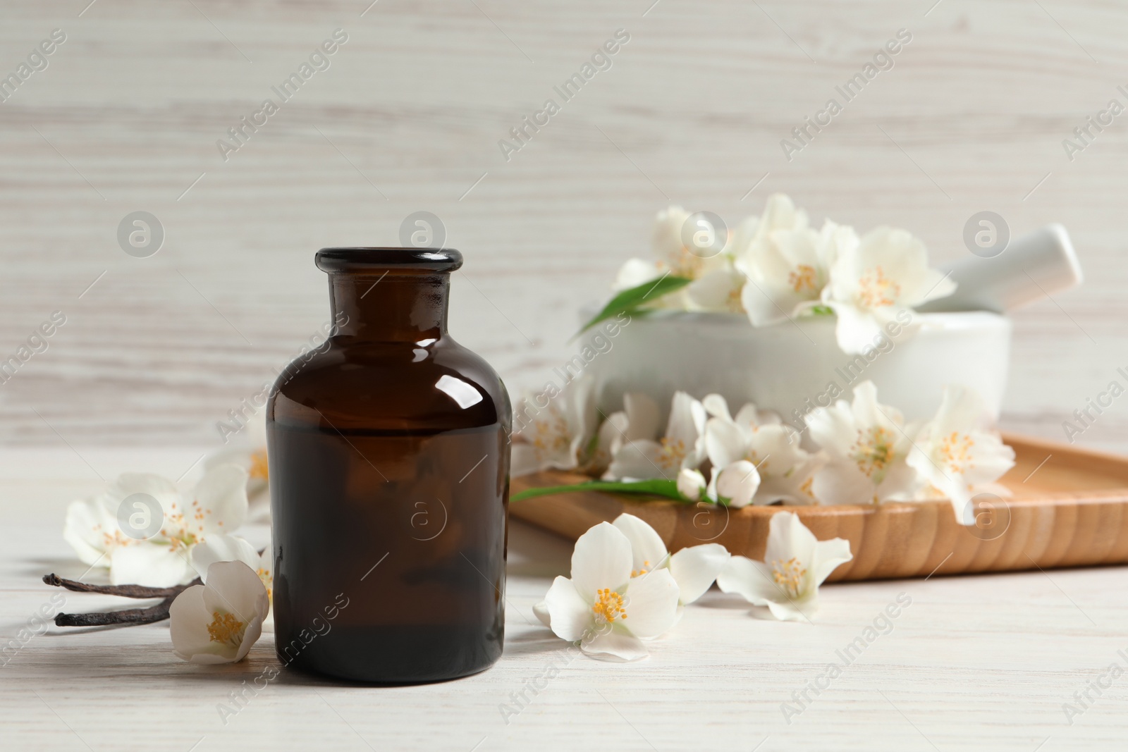 Photo of Jasmine essential oil and fresh flowers on white wooden table, space for text