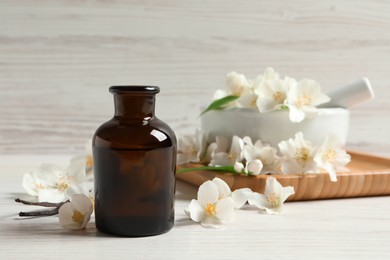 Jasmine essential oil and fresh flowers on white wooden table, space for text