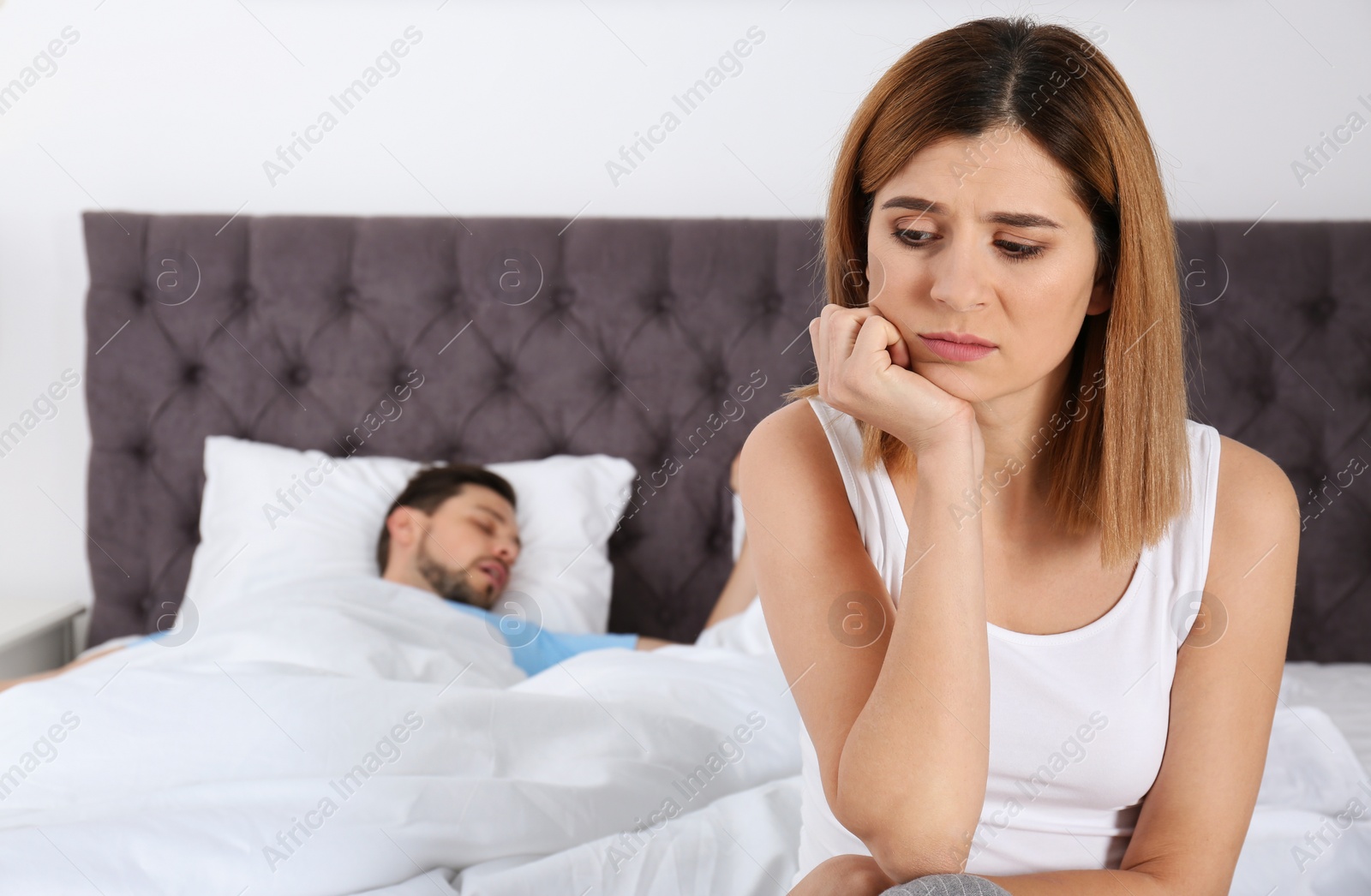 Photo of Upset woman sitting on bed near her sleeping husband at home. Relationship problems