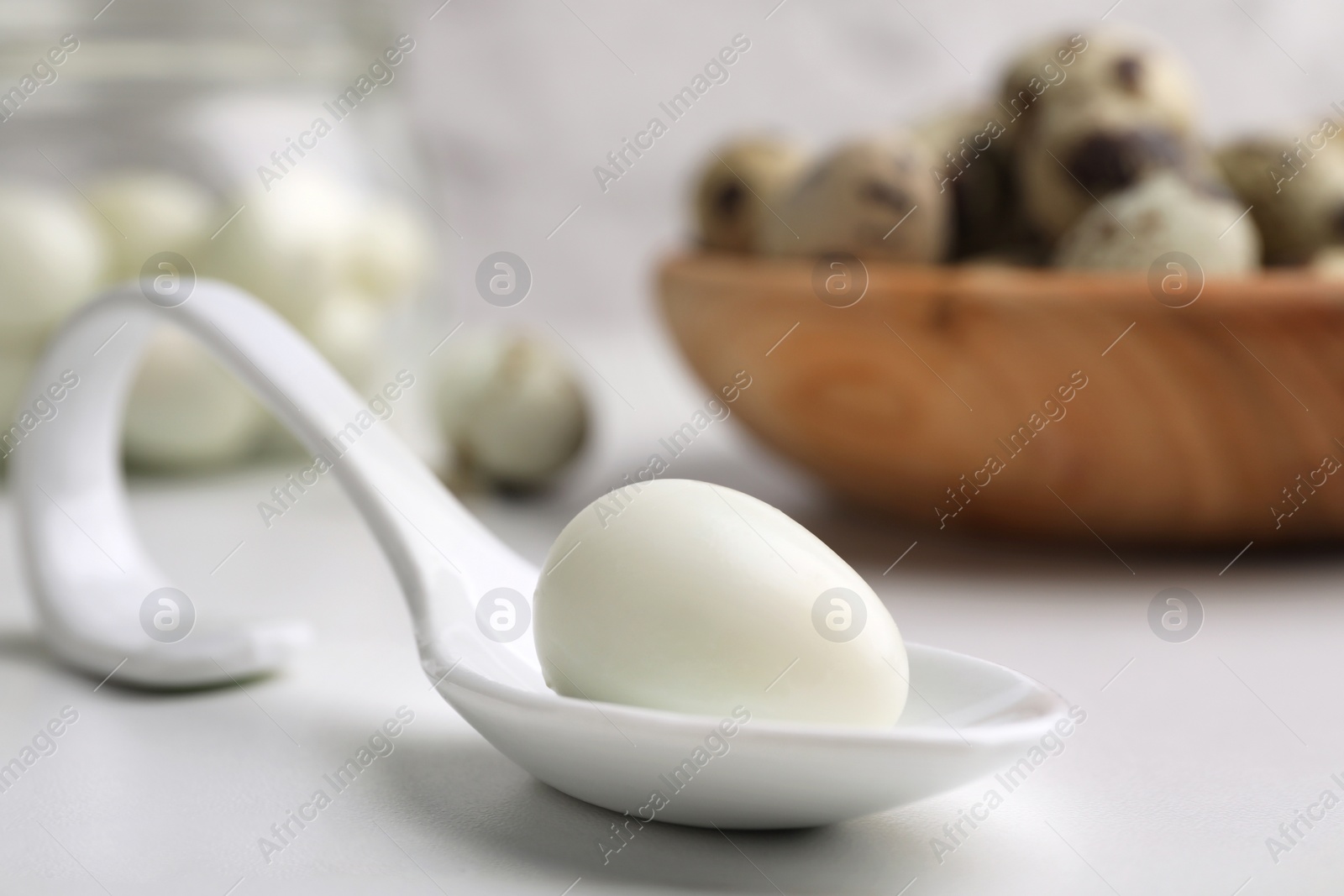 Photo of One boiled quail egg in spoon on white table, closeup. Space for text