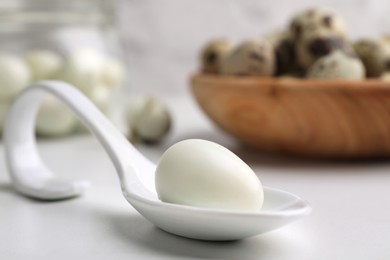 One boiled quail egg in spoon on white table, closeup. Space for text