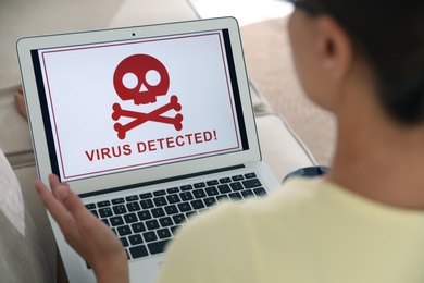 Photo of Woman using laptop with warning about virus attack on screen at home, closeup