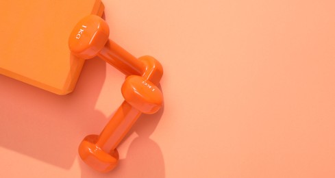 Photo of Dumbbells and yoga block on coral background, flat lay. Space for text