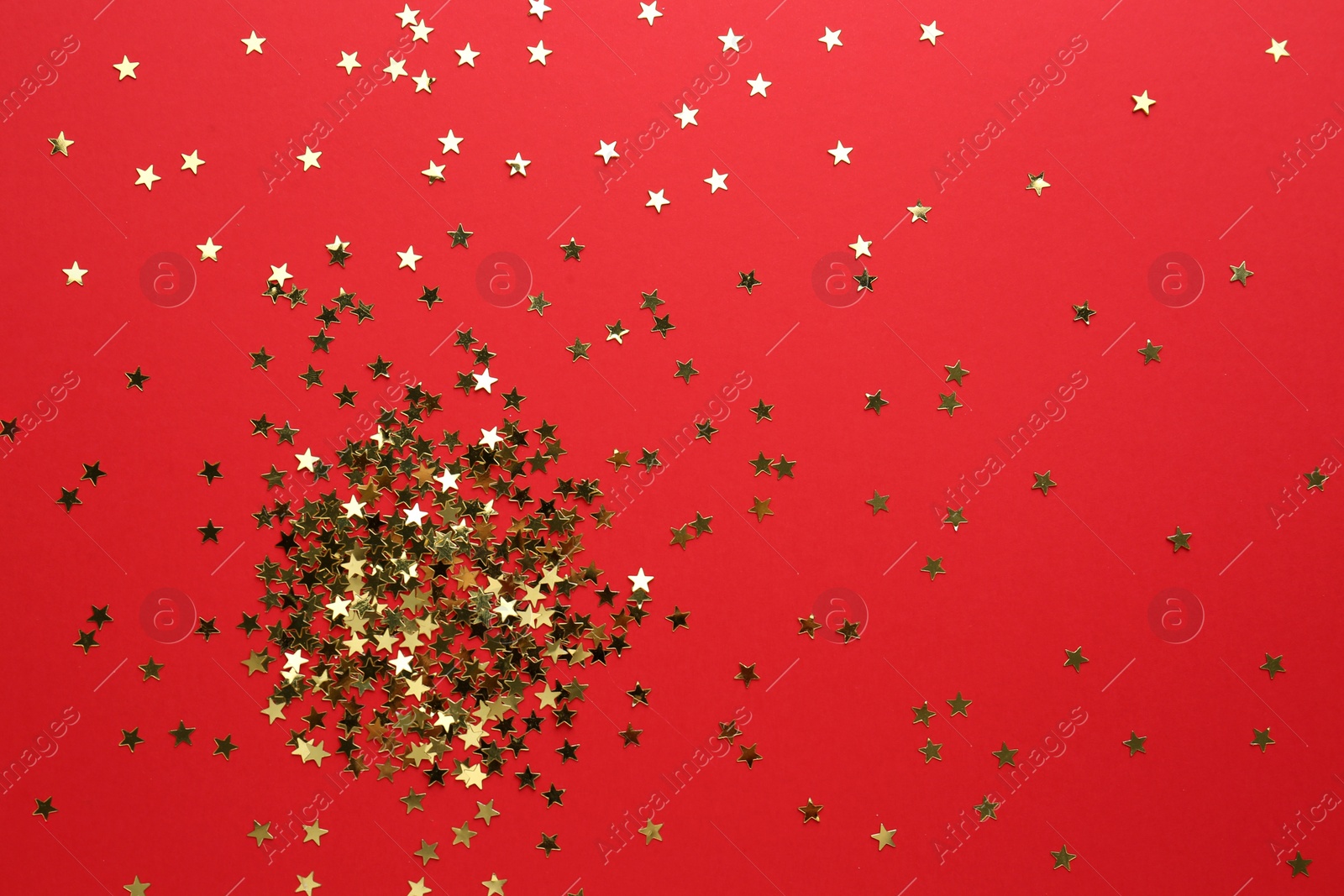 Photo of Gold confetti stars on red background, flat lay. Christmas celebration