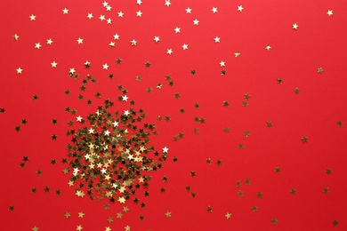 Photo of Gold confetti stars on red background, flat lay. Christmas celebration