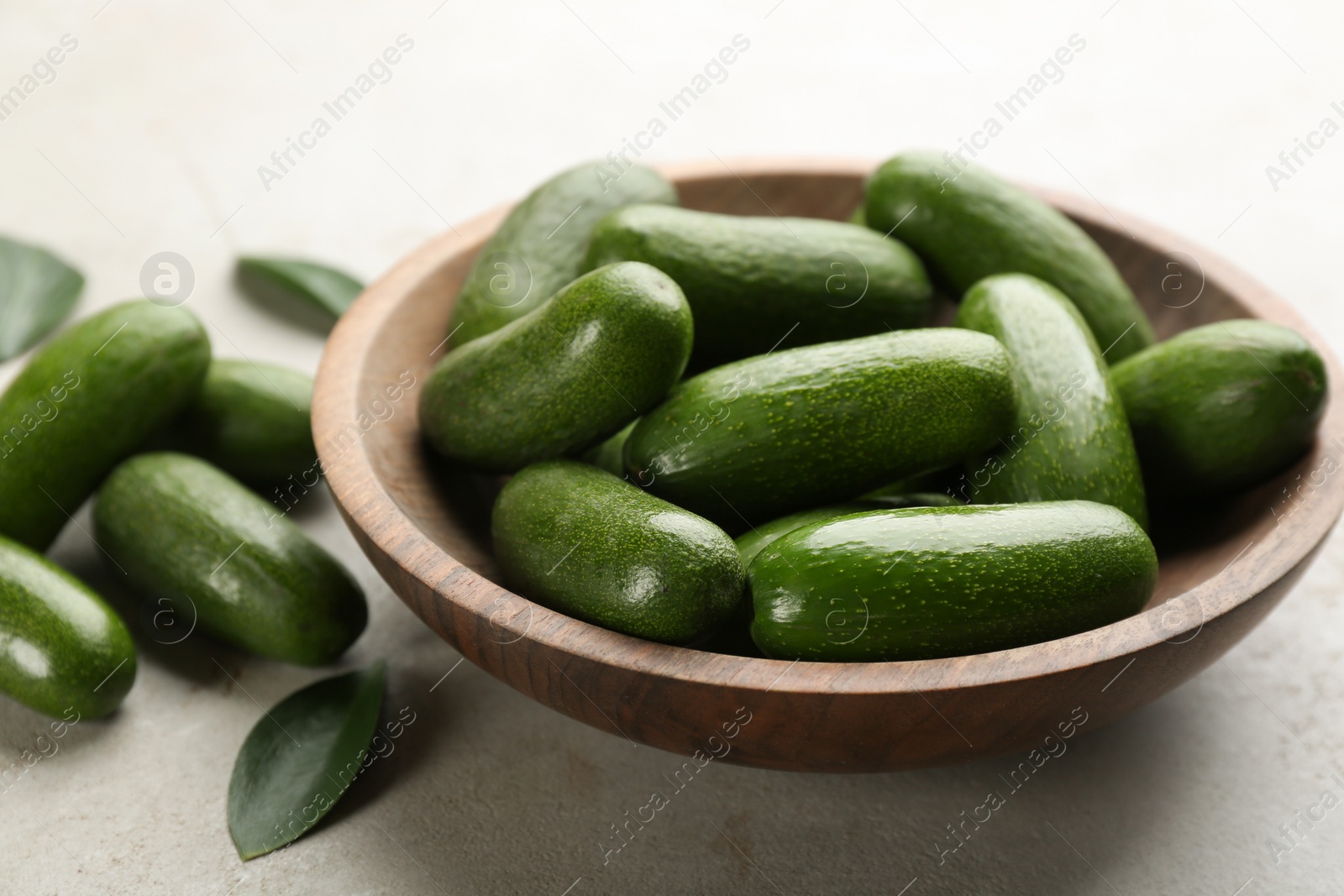 Photo of Wooden bowl with seedless avocados on grey table, closeup