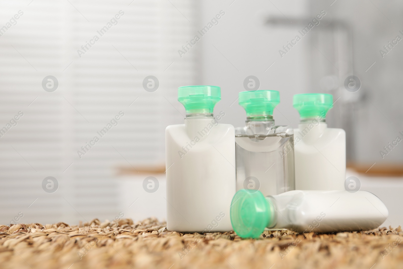 Photo of Mini bottles of cosmetic products on wicker mat against blurred background. Space for text