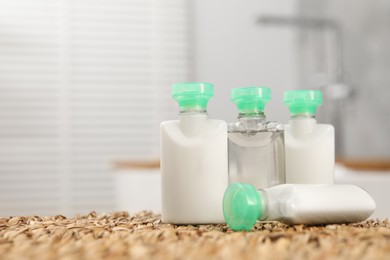 Mini bottles of cosmetic products on wicker mat against blurred background. Space for text