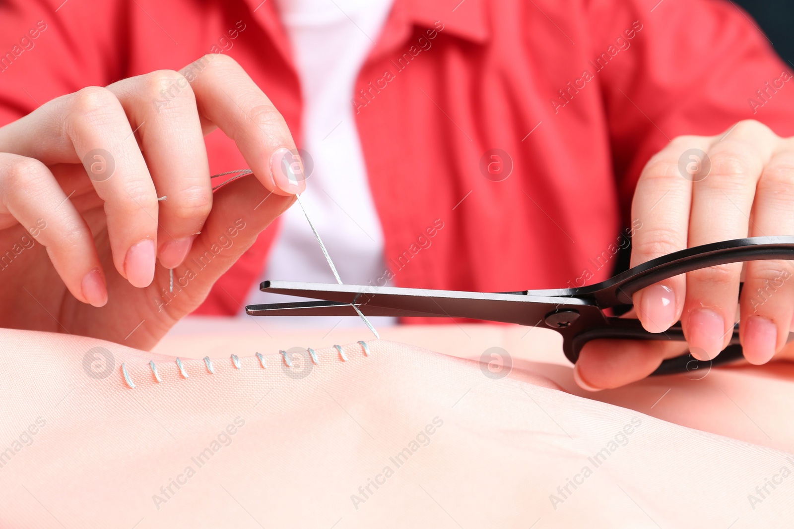 Photo of Woman cutting sewing thread over cloth, closeup