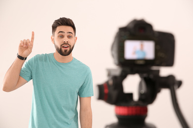 Photo of Young blogger recording video on camera against white background