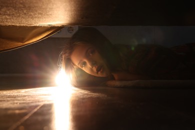 Photo of Little girl with flashlight looking for monster under bed at night