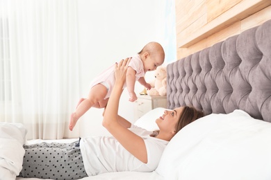 Young mother playing with her cute baby on bed indoors