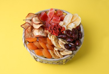 Photo of Wicker basket with different dried fruits on yellow background