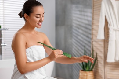 Photo of Young woman applying aloe gel onto her arm in bathroom. Space for text