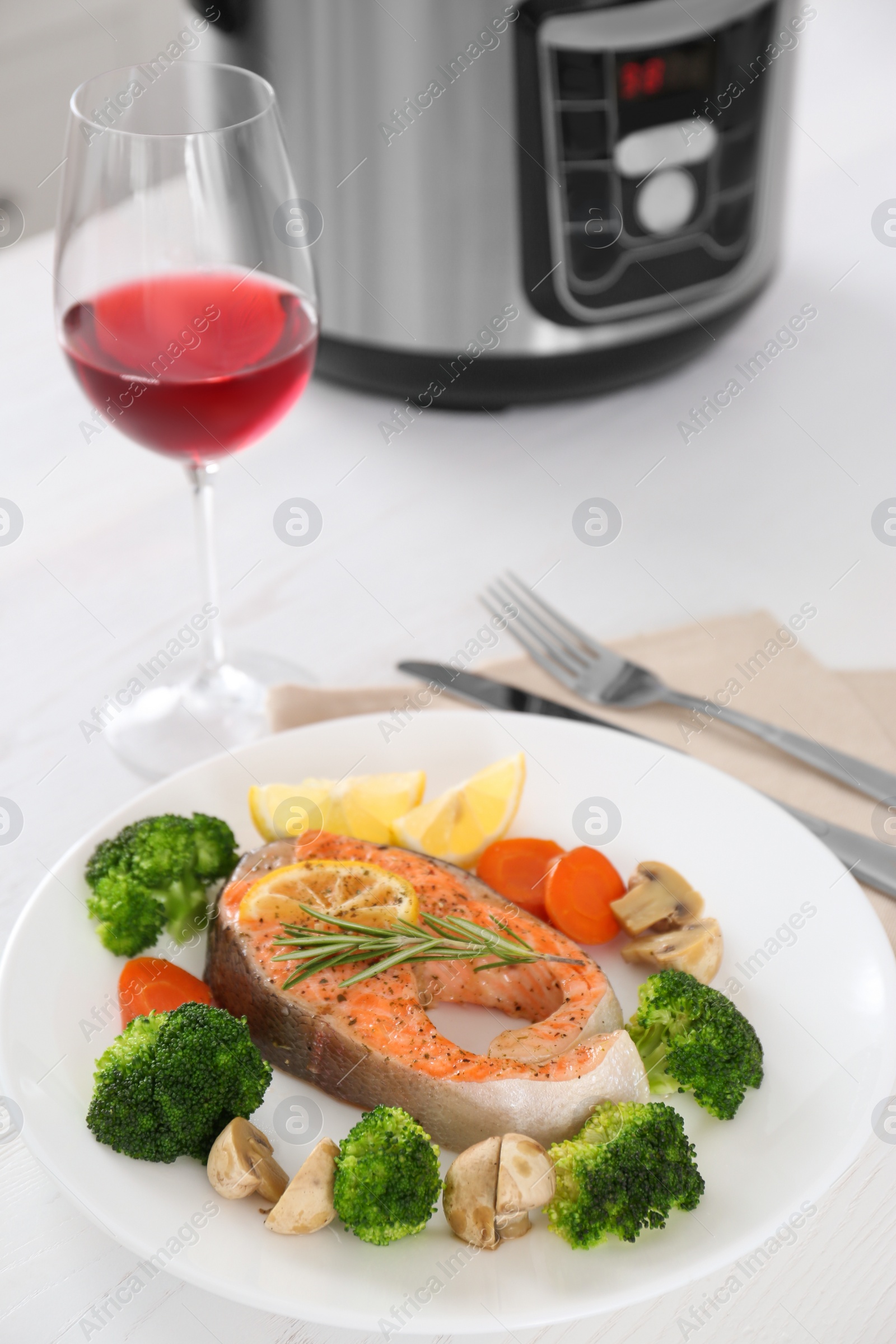 Photo of Plate with salmon steak and garnish prepared in multi cooker on table