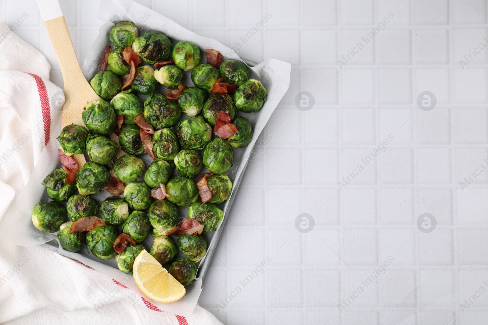 Photo of Delicious roasted Brussels sprouts, bacon and lemon in baking dish on white tiled table, top view. Space for text