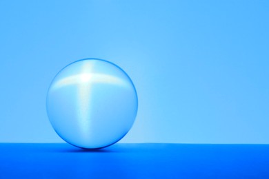 Photo of Transparent glass ball on table against light blue background. Space for text