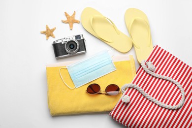 Stylish bag with beach accessories and protective mask on white background, flat lay